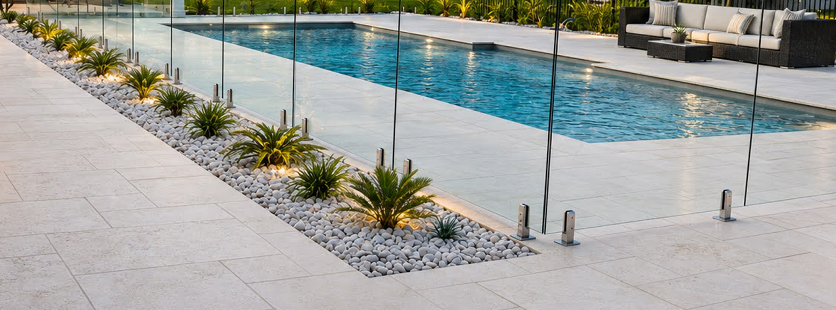 Light natural stone paving around a swimming pool with glass fencing