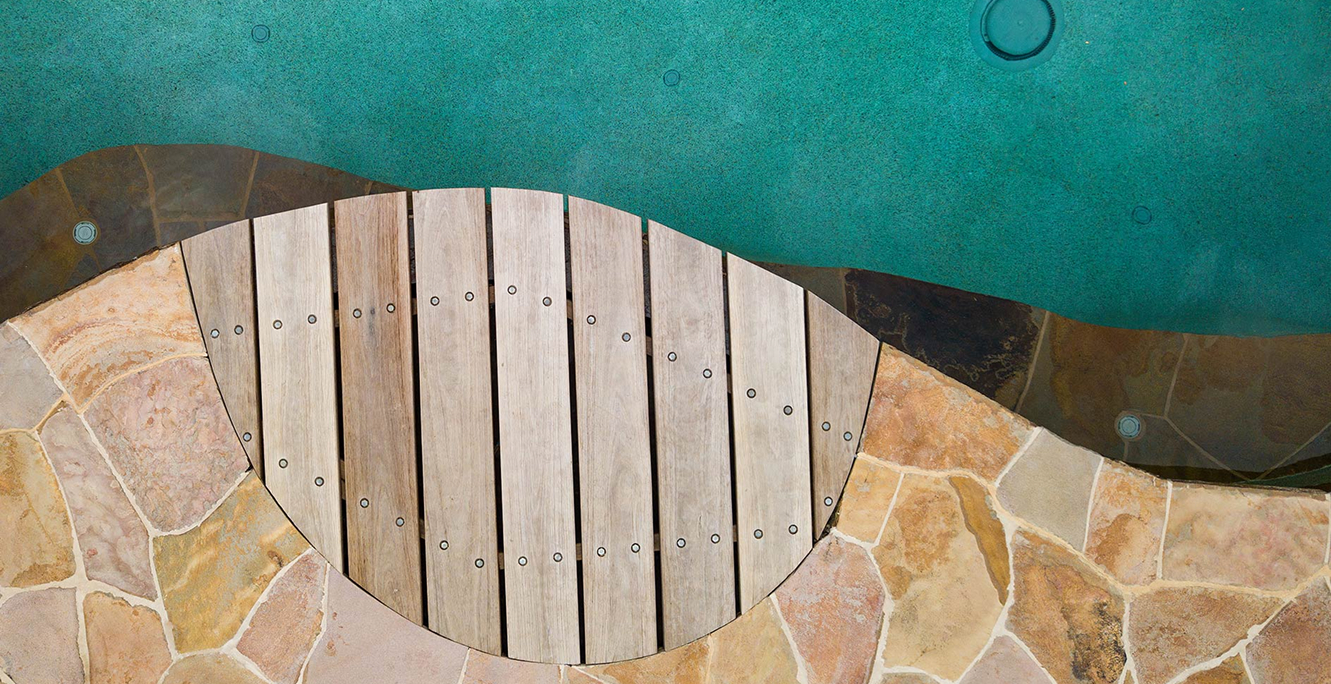 Overhead detail of curved natural stone pool coping beside a timber deck