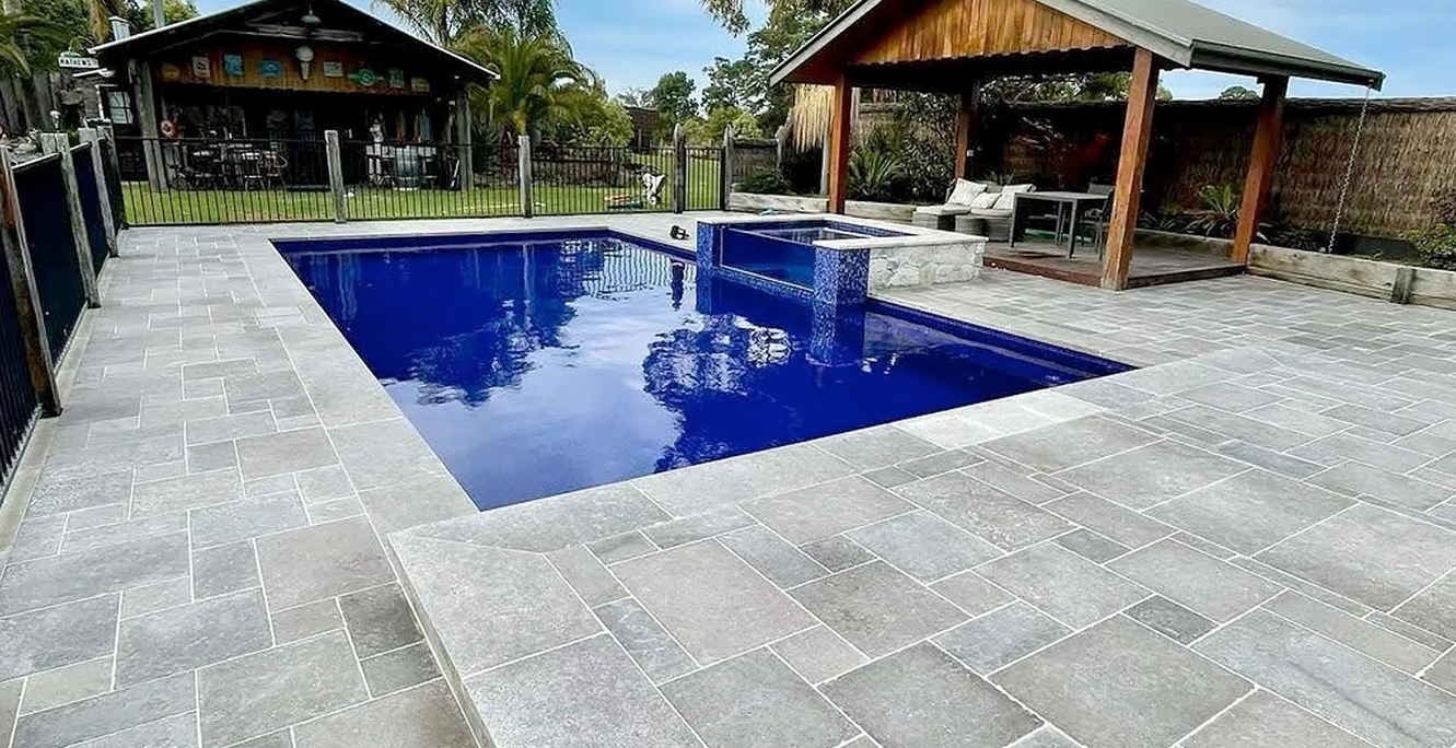 Grey natural stone paving surrounding a blue swimming pool and raised spa